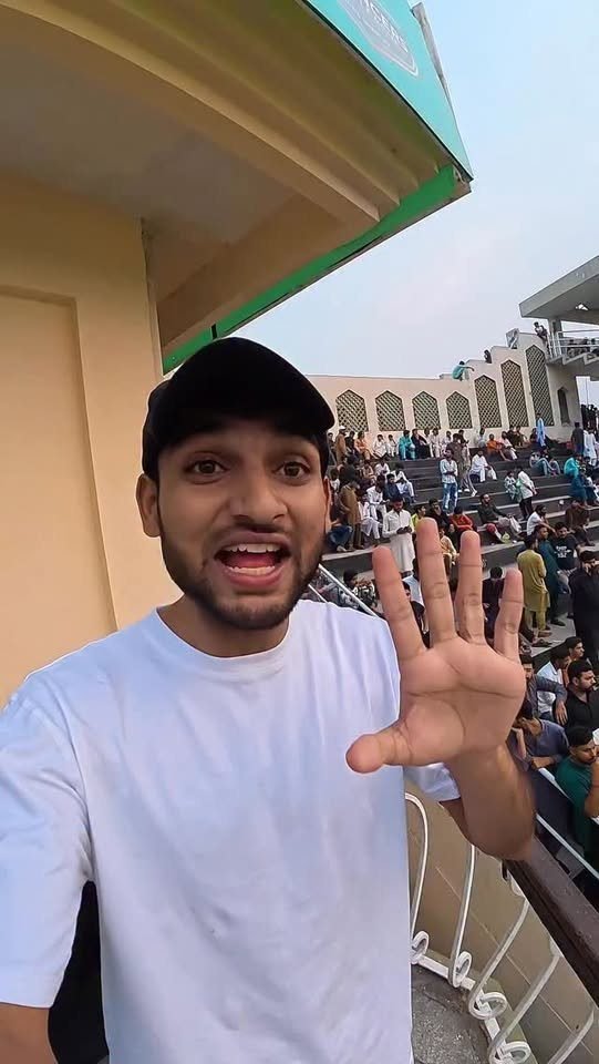 Waleed waving from a stadium stand in a white t-shirt and cap