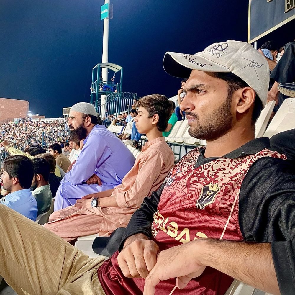 Waleed sitting in the stands at a floodlit cricket match