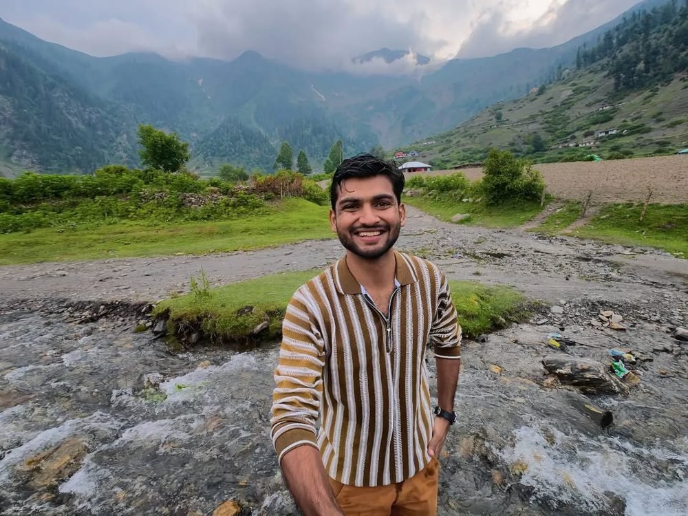 Waleed Ahmad standing by a river in Kaghan valley, Pakistan, mountains behind him