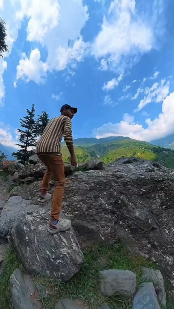 Waleed climbing a boulder on a hillside in Kaghan valley under a blue sky